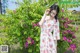 A woman standing in front of a bush of flowers.