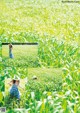 A woman in a blue dress and hat walking through a field of green grass.