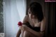 A woman sitting on a window sill holding a red rose.