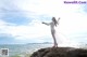 A woman in a white dress standing on a rock by the ocean.