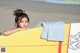 A woman leaning on a yellow surfboard on the beach.