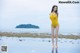 A woman in a yellow bathing suit standing on a beach.